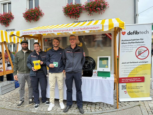 defibtech Messestand bei der Ortsbildmesse Kleinzell 2026: Dr. Michael Haider (Intensivmediziner und Feuerwehrarzt), Carina Hollnsteiner, Andreas Höllinger und Kevin Rottinger (Fachbeauftragter FMD) präsentieren gemeinsam einen Defibrillator und informieren über moderne Erste-Hilfe- und Notfallmedizin. Im Hintergrund sind weitere Defibrillator-Modelle sowie der Messestand von defibtech zu sehen.